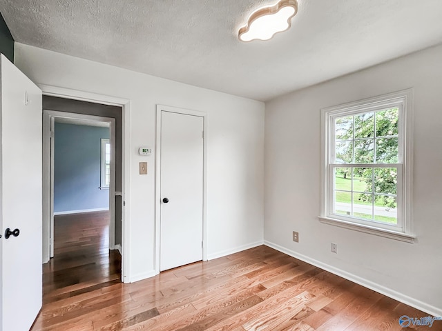 unfurnished room with light wood-type flooring, a textured ceiling, and baseboards