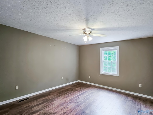 spare room featuring a textured ceiling, dark wood-style flooring, visible vents, a ceiling fan, and baseboards