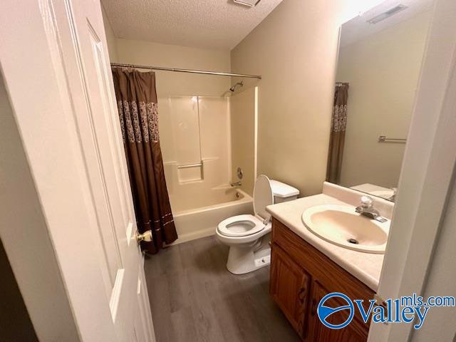 full bathroom featuring a textured ceiling, shower / bathtub combination with curtain, wood-type flooring, toilet, and vanity