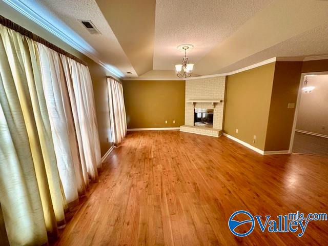 unfurnished living room with ornamental molding, a brick fireplace, wood-type flooring, and an inviting chandelier