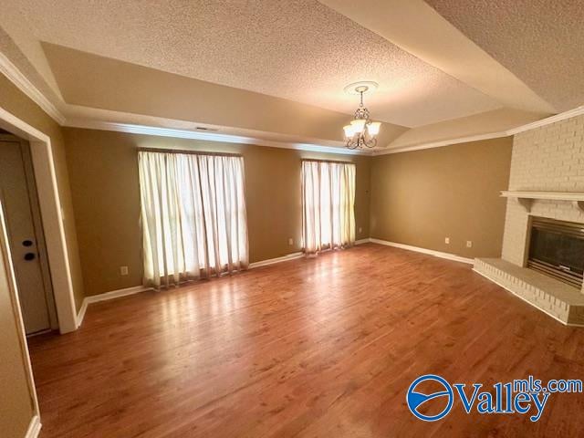 unfurnished living room featuring a fireplace, a textured ceiling, hardwood / wood-style floors, crown molding, and an inviting chandelier