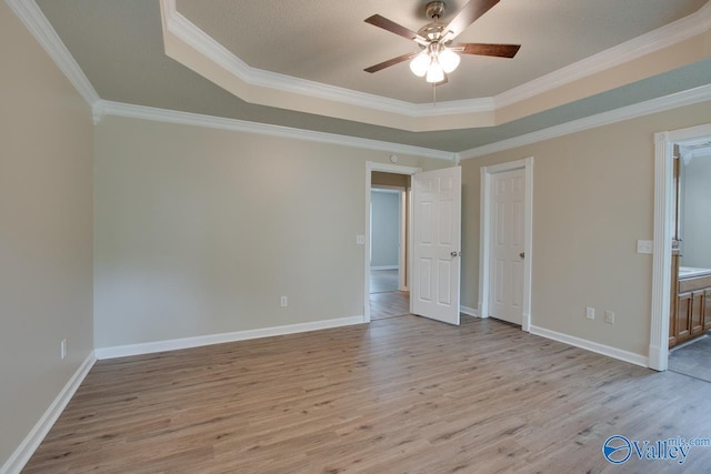 unfurnished bedroom with a tray ceiling, light wood-style floors, crown molding, and baseboards