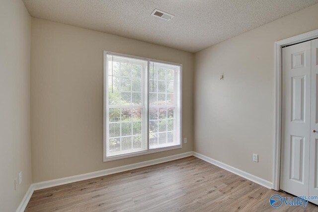 unfurnished room featuring light wood finished floors, baseboards, and a textured ceiling