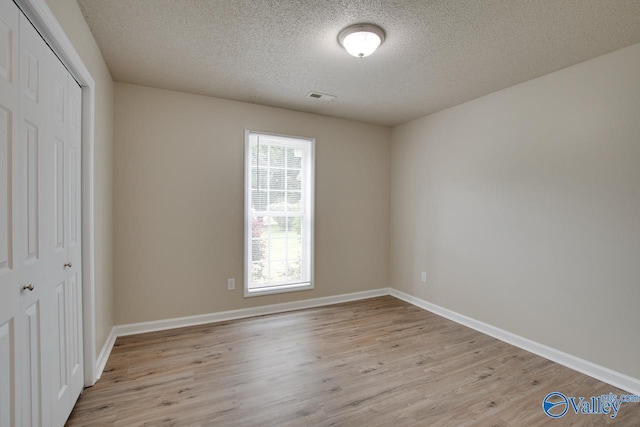 unfurnished bedroom featuring a closet, light wood-style flooring, a textured ceiling, and baseboards