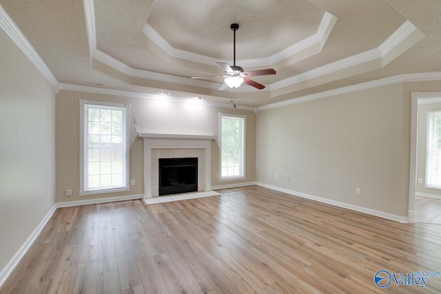 unfurnished living room featuring a raised ceiling, healthy amount of natural light, ceiling fan, light wood-type flooring, and ornamental molding