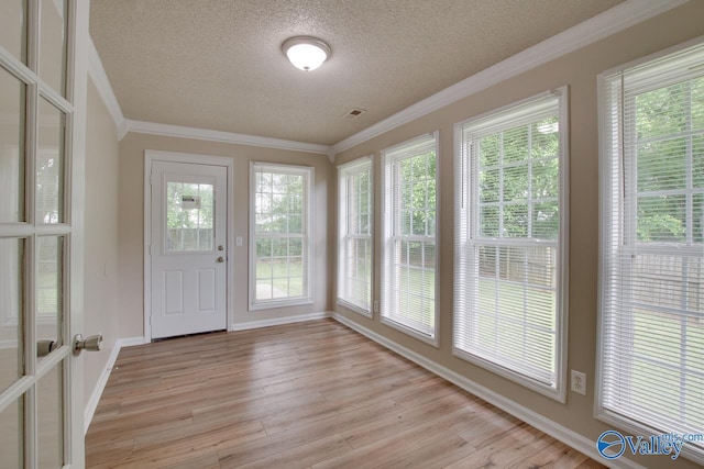 unfurnished sunroom featuring a textured ceiling, plenty of natural light, wood finished floors, crown molding, and baseboards