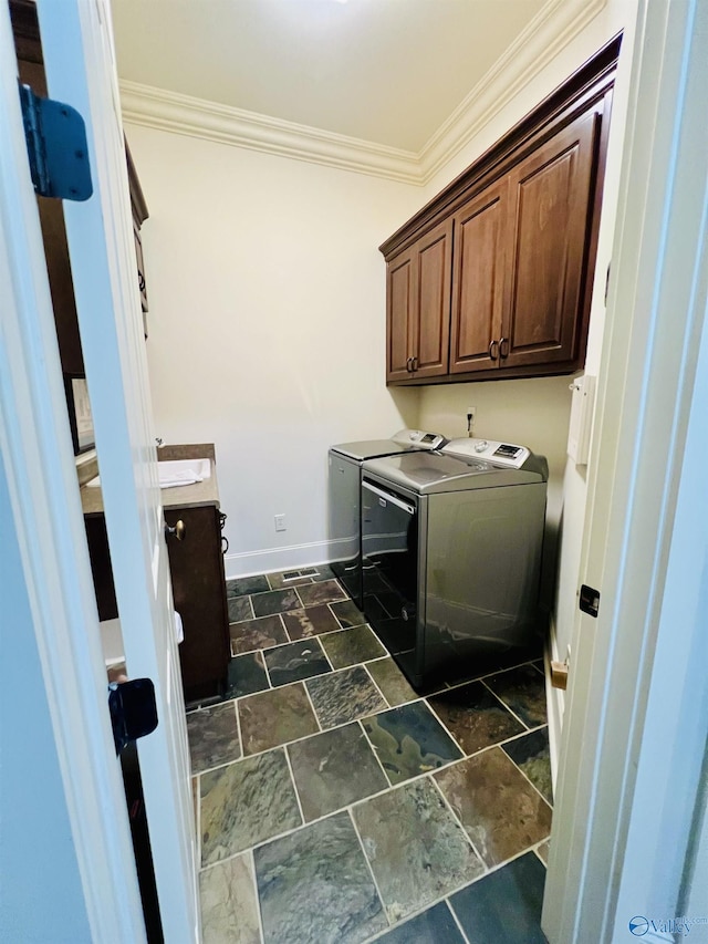 clothes washing area featuring cabinets, crown molding, and washing machine and clothes dryer