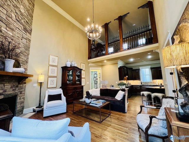 living room with a stone fireplace, a towering ceiling, a chandelier, crown molding, and light hardwood / wood-style flooring