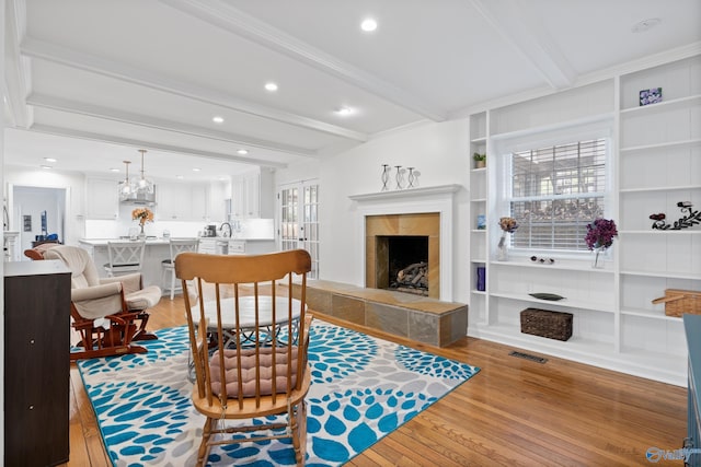 living room featuring beam ceiling, built in shelves, a high end fireplace, crown molding, and light wood-type flooring