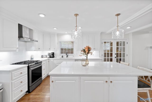 kitchen with a center island, sink, hanging light fixtures, wall chimney exhaust hood, and stainless steel gas stove