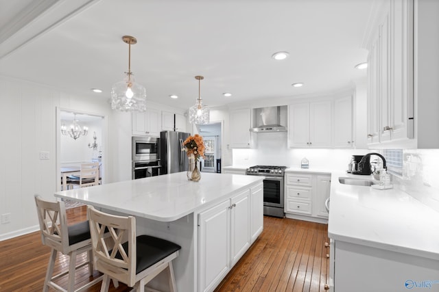 kitchen with wall chimney exhaust hood, stainless steel appliances, sink, white cabinets, and a kitchen island