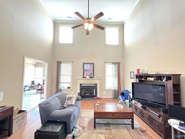 living room featuring a wealth of natural light, light hardwood / wood-style flooring, crown molding, and a high ceiling