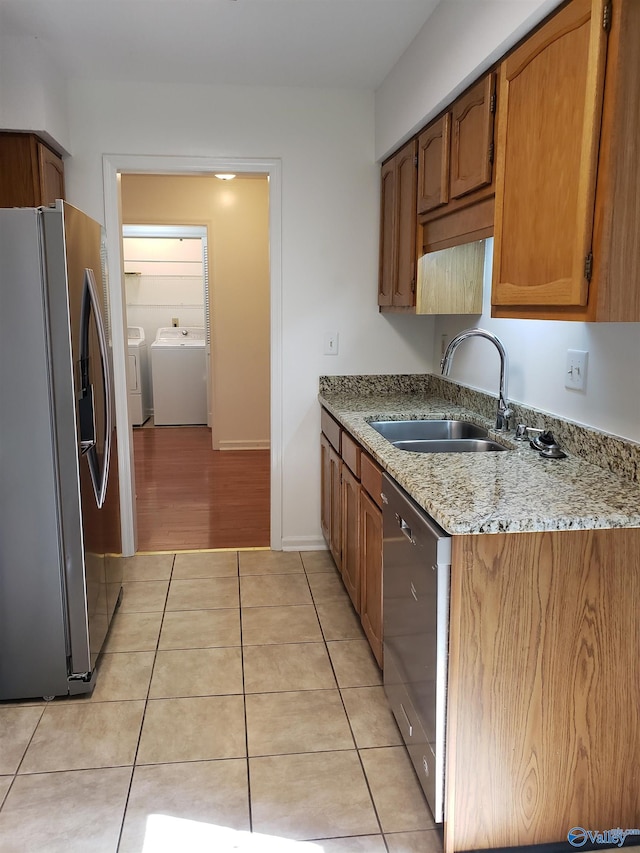 kitchen featuring light stone counters, stainless steel appliances, sink, light tile patterned floors, and washing machine and dryer