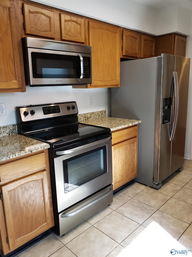 kitchen featuring light tile patterned flooring, light stone counters, and stainless steel appliances