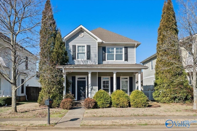 traditional-style house featuring covered porch, a shingled roof, and fence