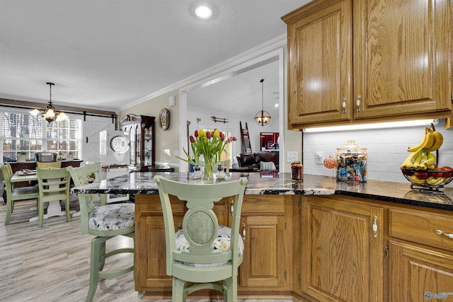 kitchen featuring a barn door, ornamental molding, brown cabinetry, and dark stone countertops