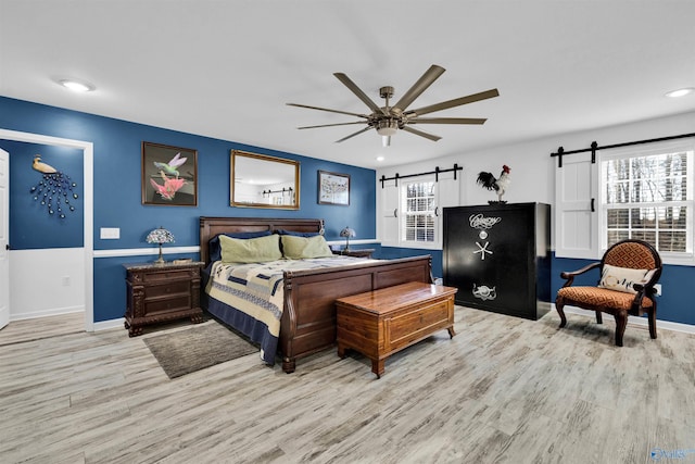 bedroom with light wood finished floors, a barn door, and multiple windows