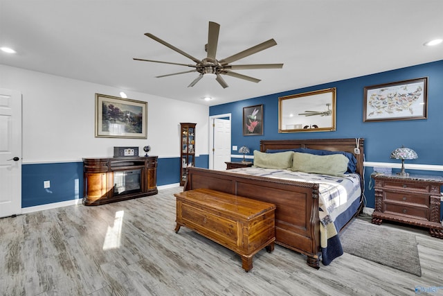 bedroom with a glass covered fireplace, wood finished floors, a ceiling fan, and recessed lighting