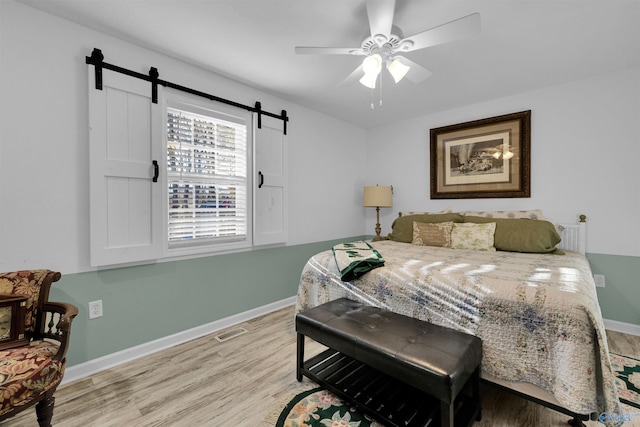 bedroom featuring light wood-style floors, a barn door, visible vents, and baseboards