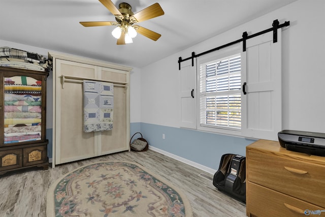 home office featuring light wood-type flooring, a barn door, baseboards, and ceiling fan