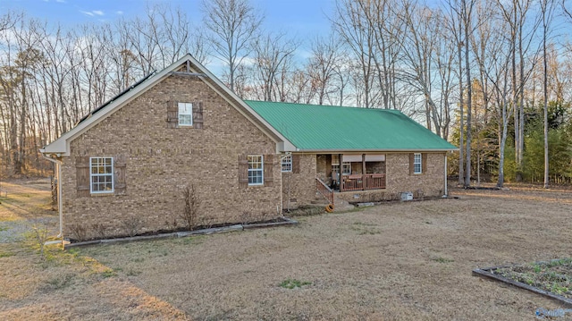 view of front facade with covered porch, brick siding, metal roof, and driveway