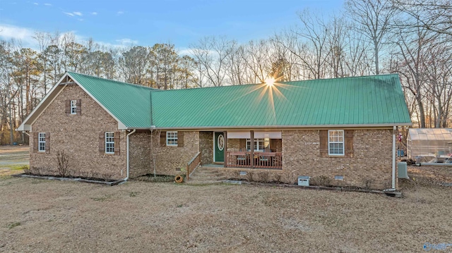 rear view of house with metal roof, a porch, a greenhouse, brick siding, and crawl space