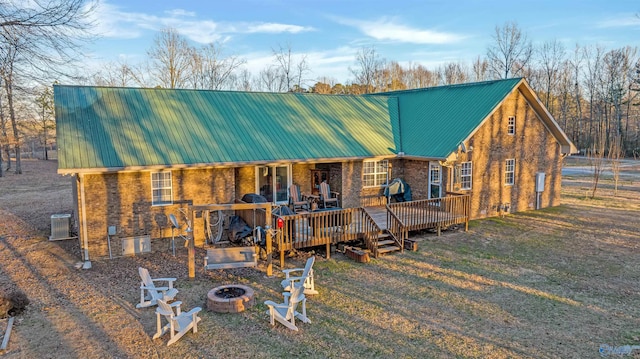 rustic home featuring an outdoor fire pit, brick siding, metal roof, and central AC unit