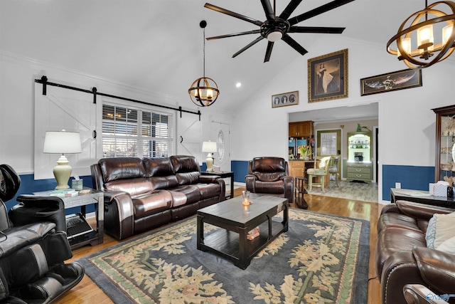 living room with high vaulted ceiling, ceiling fan with notable chandelier, wood finished floors, and a barn door