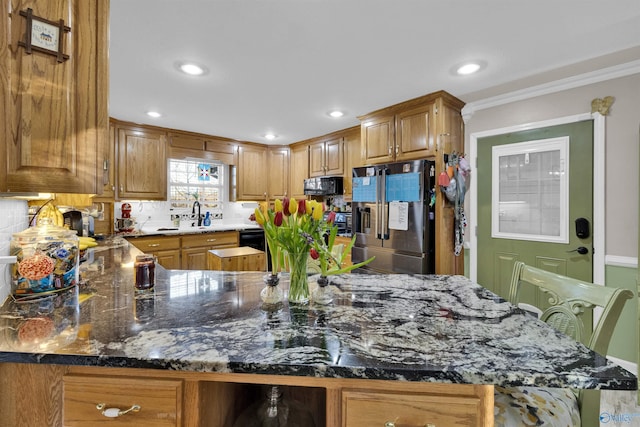 kitchen with stainless steel fridge, stone countertops, brown cabinets, black microwave, and a sink