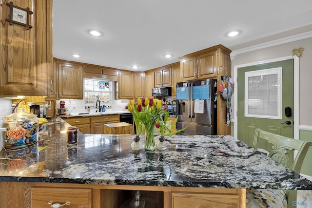 kitchen featuring brown cabinets, recessed lighting, dark stone counters, black microwave, and stainless steel fridge