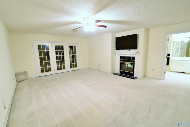 unfurnished living room with french doors, ceiling fan, a textured ceiling, a fireplace, and light colored carpet