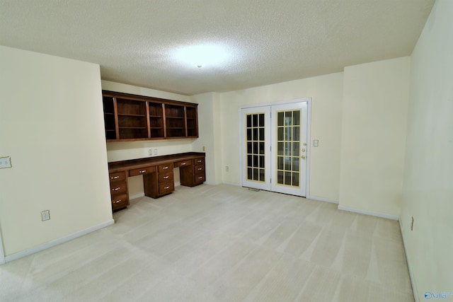 kitchen featuring dark brown cabinetry, french doors, light colored carpet, a textured ceiling, and built in desk