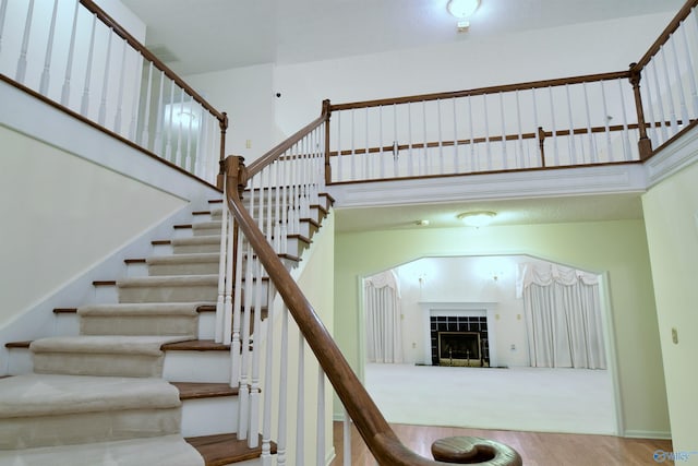 staircase with wood-type flooring, a fireplace, and a high ceiling