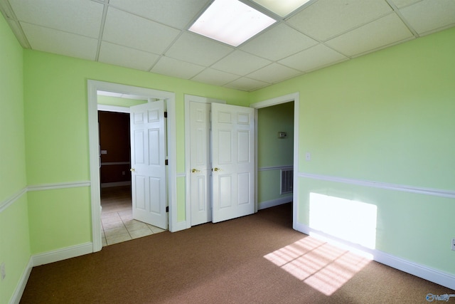 unfurnished bedroom featuring a drop ceiling and light colored carpet