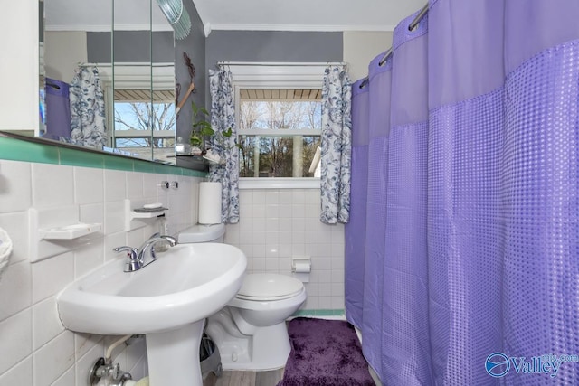 bathroom with toilet, crown molding, and tile walls