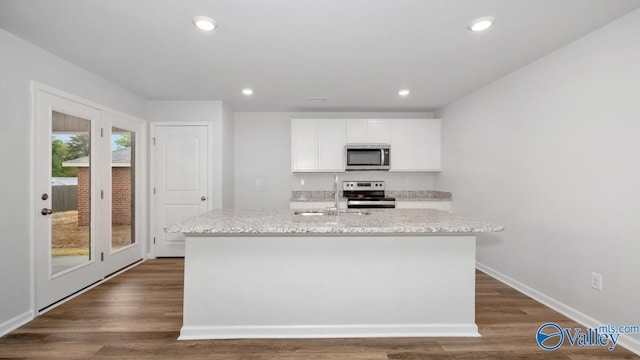 kitchen with white cabinetry, light stone countertops, dark hardwood / wood-style flooring, a center island with sink, and appliances with stainless steel finishes