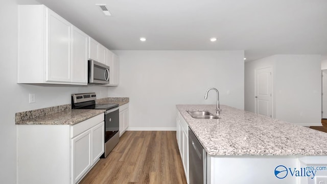 kitchen with a kitchen island with sink, white cabinets, sink, light hardwood / wood-style flooring, and appliances with stainless steel finishes