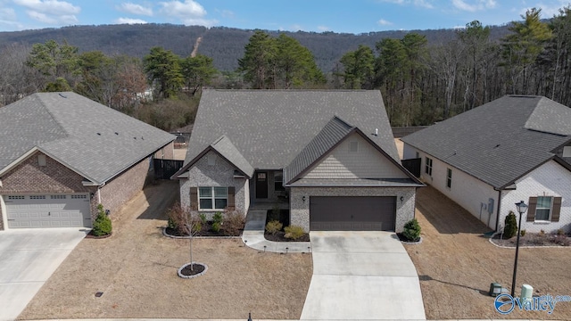 view of front of home with driveway, an attached garage, a wooded view, and brick siding