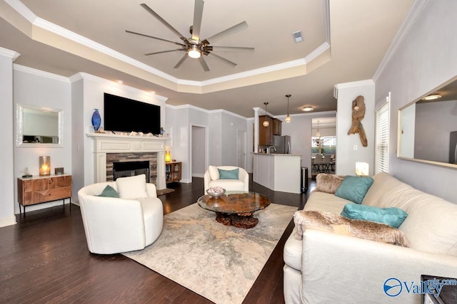 2906 Pasture View Ln, Owens Cross Roads, AL 35763 - living room featuring a raised ceiling, a ceiling fan, dark wood-style flooring, a stone fireplace, and ornamental molding