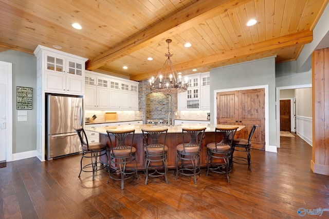 kitchen with a kitchen island with sink, pendant lighting, white cabinetry, stainless steel refrigerator, and dark hardwood / wood-style flooring