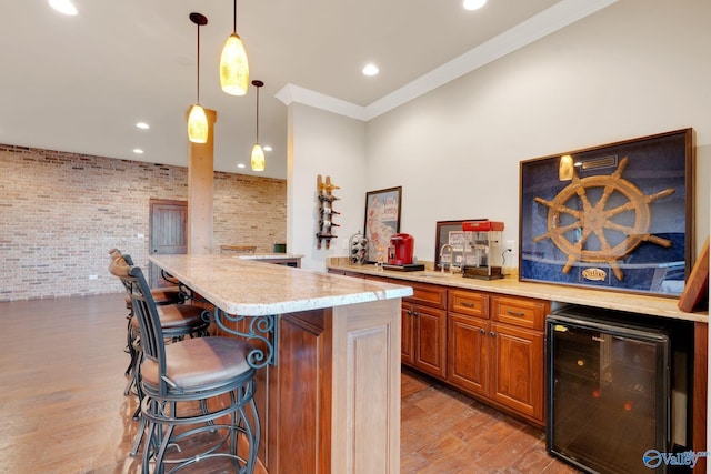 kitchen featuring wine cooler, light stone countertops, a kitchen bar, light hardwood / wood-style floors, and brick wall