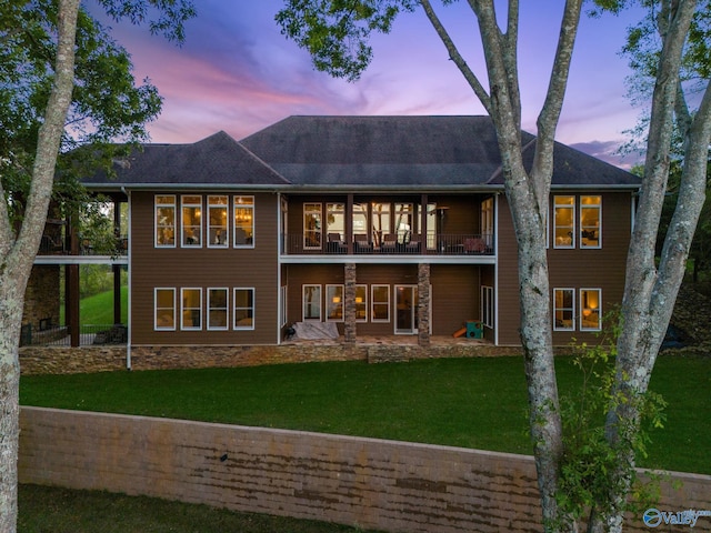 back house at dusk featuring a balcony, a yard, and a patio