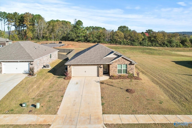 view of front of home with a front lawn, driveway, central AC, brick siding, and an attached garage