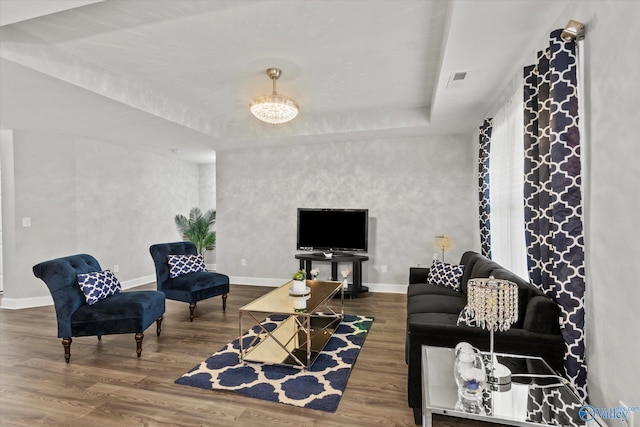 living room featuring a raised ceiling, wood finished floors, visible vents, and baseboards