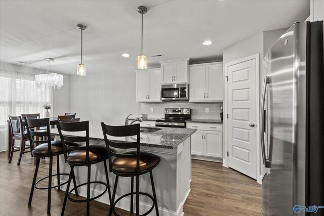 kitchen featuring a sink, white cabinetry, a notable chandelier, appliances with stainless steel finishes, and a breakfast bar area