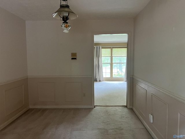 empty room featuring wainscoting, light carpet, and a decorative wall