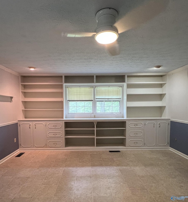 unfurnished room featuring a textured ceiling, baseboards, a ceiling fan, and built in shelves