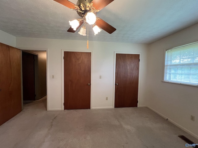 unfurnished bedroom with light colored carpet, two closets, visible vents, and baseboards