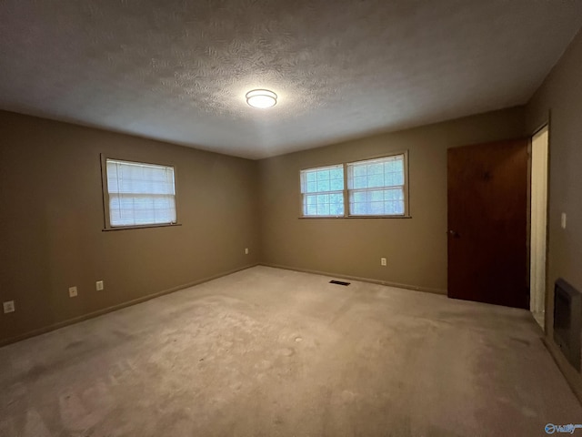 carpeted empty room with a textured ceiling, baseboards, and visible vents