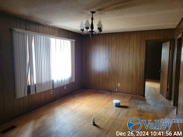 empty room featuring wood walls, hardwood / wood-style flooring, a textured ceiling, and an inviting chandelier